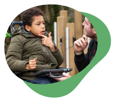 A child and his carer using AAC in the park.
