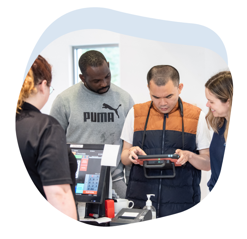 Image of a man using his Talk Pad to order food at a cafe, alongside a Smartbox team member and his support worker.