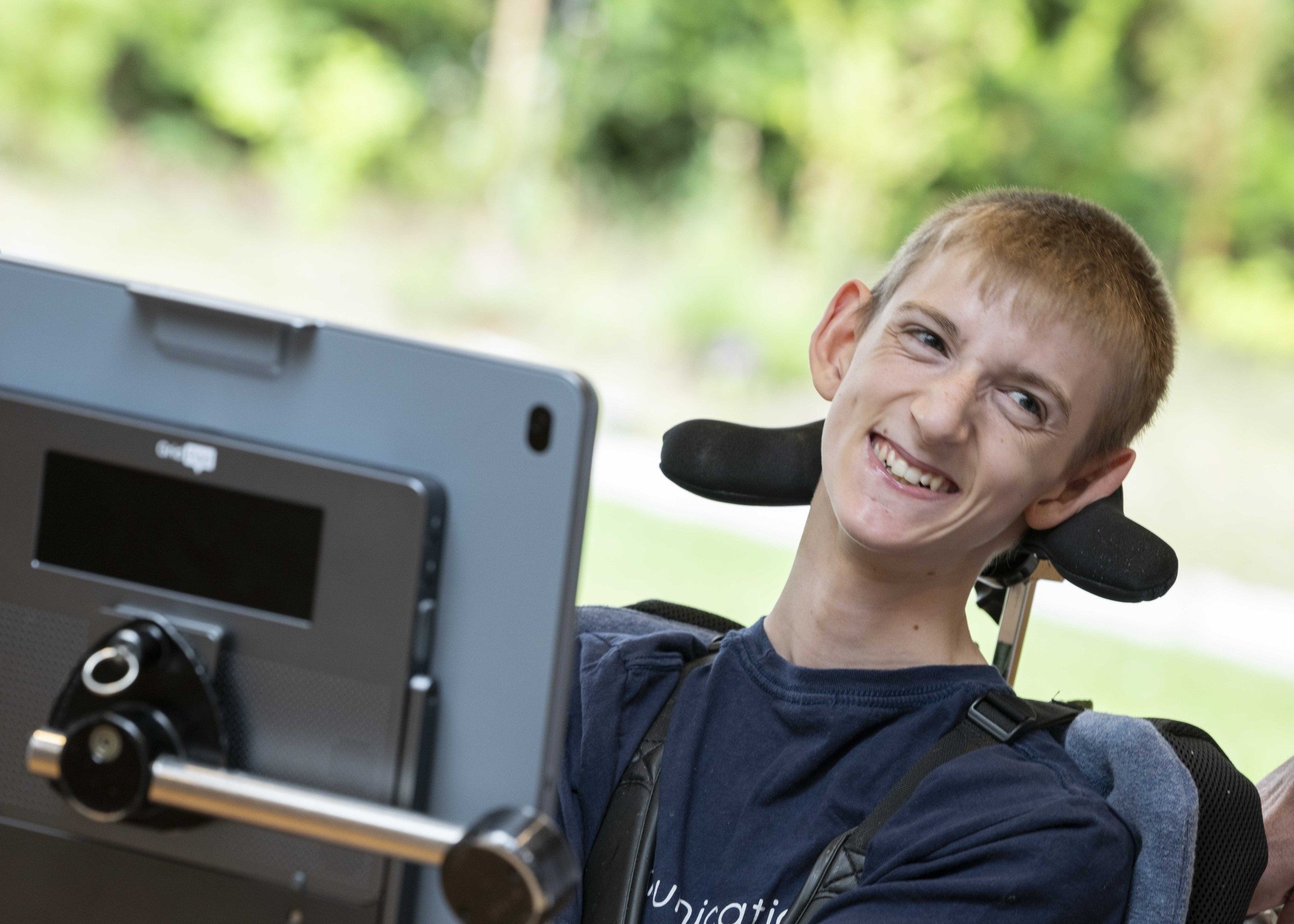 On device processing - Smartboxer Samuel smiling outdoors, trees in the background, with his Grid Pad 16 and Evo eye tracker.