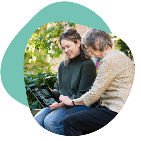Two ladies sitting on a park bench looking at a screen showing Aphasia Duo