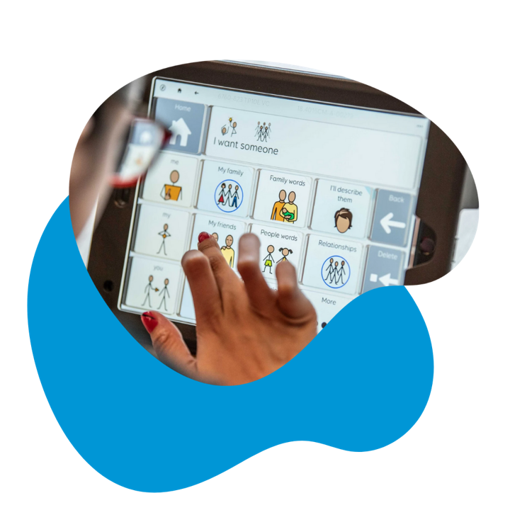 Close-up photo of a person selecting vocabulary on a Grid communication device, with buttons for family, friends, relationships, and describing people.