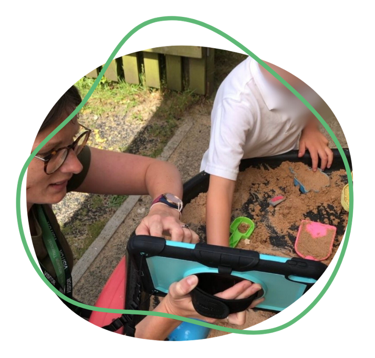 A child using a touch screen Grid Pad to communicate with an adult by a sand box