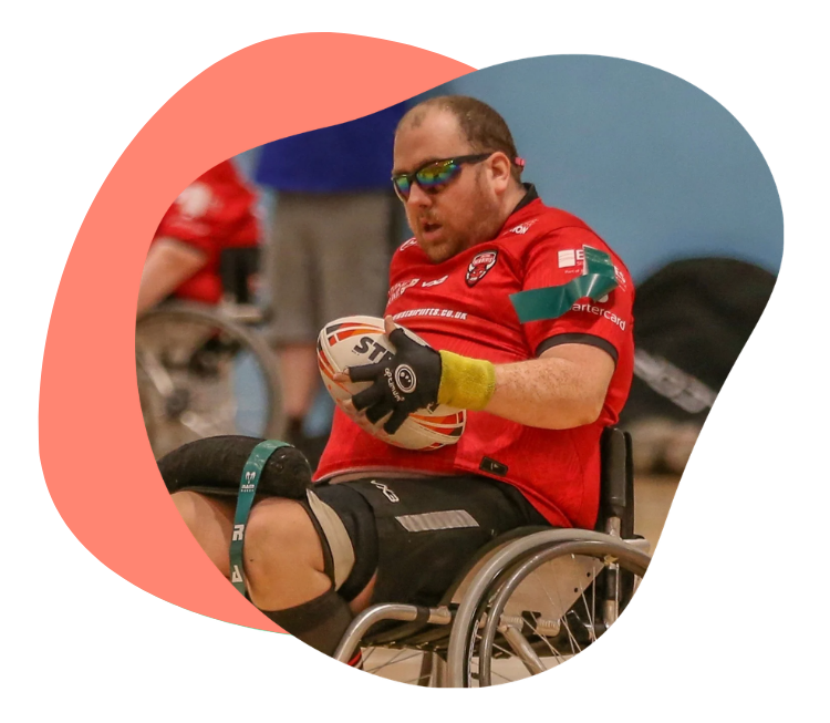 Wheelchair rugby player in a red team jersey holding a rugby ball during a match.