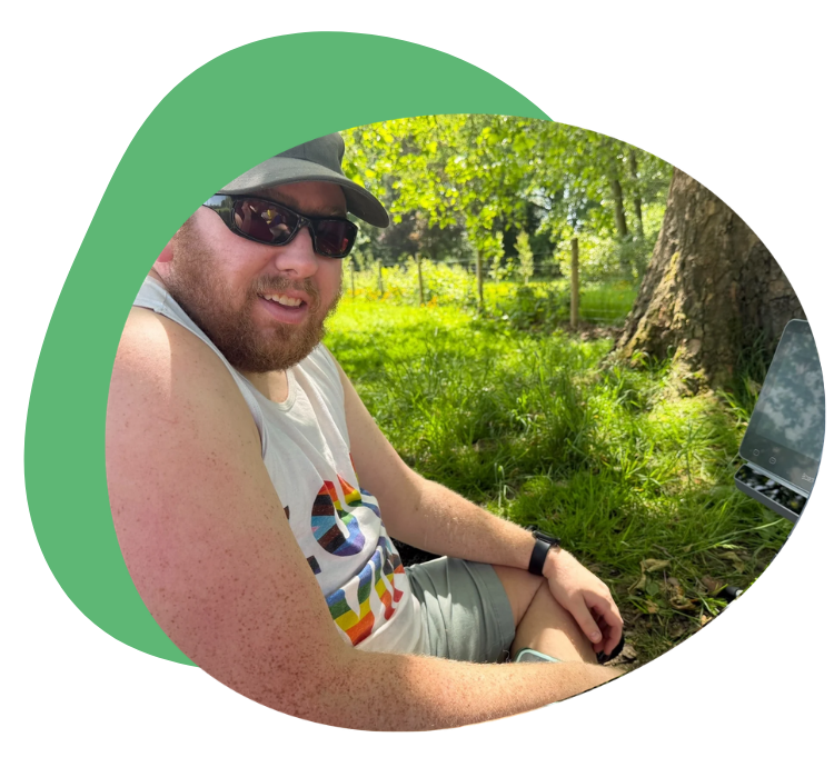 Oliver outdoors in the shade beside his Grid Pad, smiling at the camera with trees and greenery.