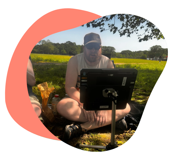 Oliver sitting outdoors in a park using a mounted communication device while relaxing