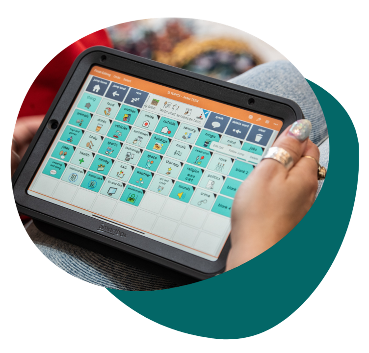 Close-up of a person holding a Smartbox communication device displaying Super Core vocabulary in Grid,