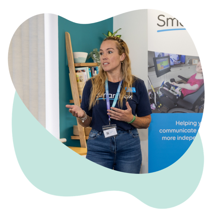 Becky delivers a presentation at an event, speaking to attendees while standing beside a Smartbox display banner