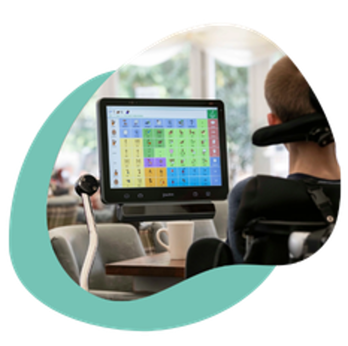 Samuel uses his mounted Grid Pad AAC device from his wheelchair. The device displays a communication Grid set.