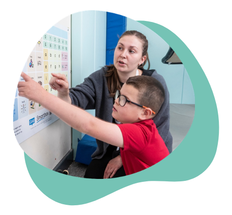 A child and a communication partner use a printed AAC communication board together. The child points to symbols on the board while the adult provides communication support